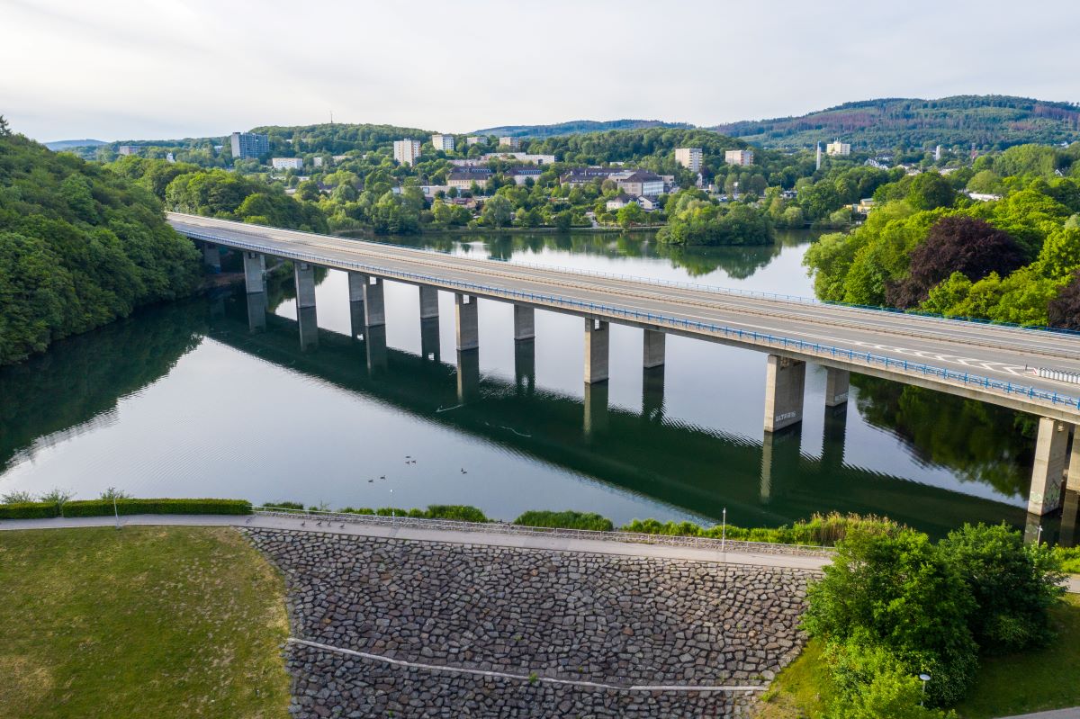 Die Natur erkunden mit gewartetem Auto dank der Werkstätten in Iserlohn Die Brücke über dem Seilersee in Iserlohn mit Wald, Gebäuden und Kfz-Werkstätten im Hintergrund.
